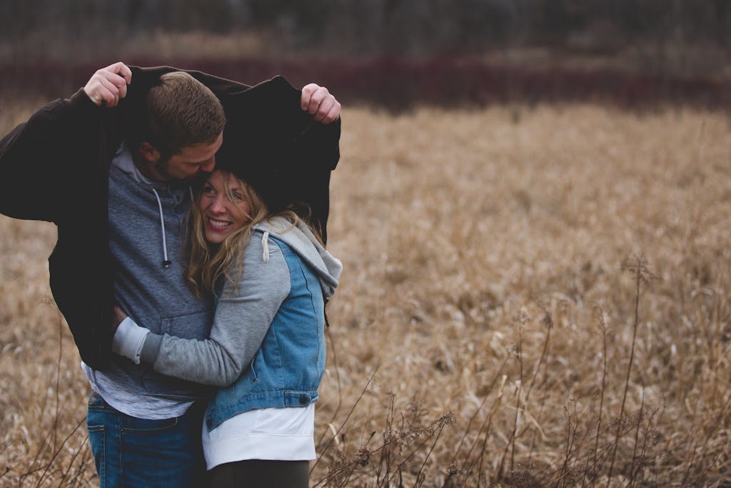 A couple shares a warm embrace under a coat in a rustic autumn field, expressing love and togetherness. dating rules