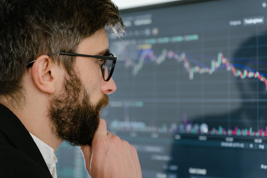 A focused man with glasses studies stock market graphs on a screen, pondering insights. beginner investing