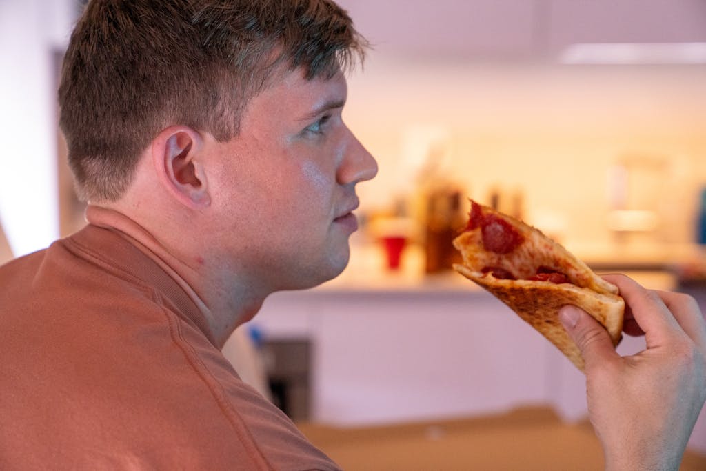 A man savors a slice of pepperoni pizza in a warmly lit indoor setting, side view emphasized. ghosting someone