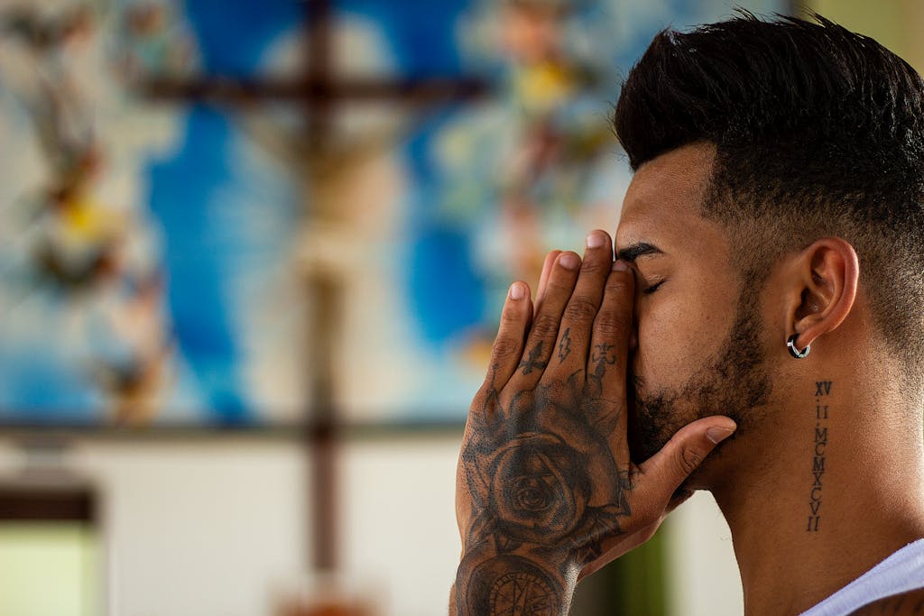 A man with tattoos prays inside a church, capturing a moment of reflection and spirituality. men's mental health awareness