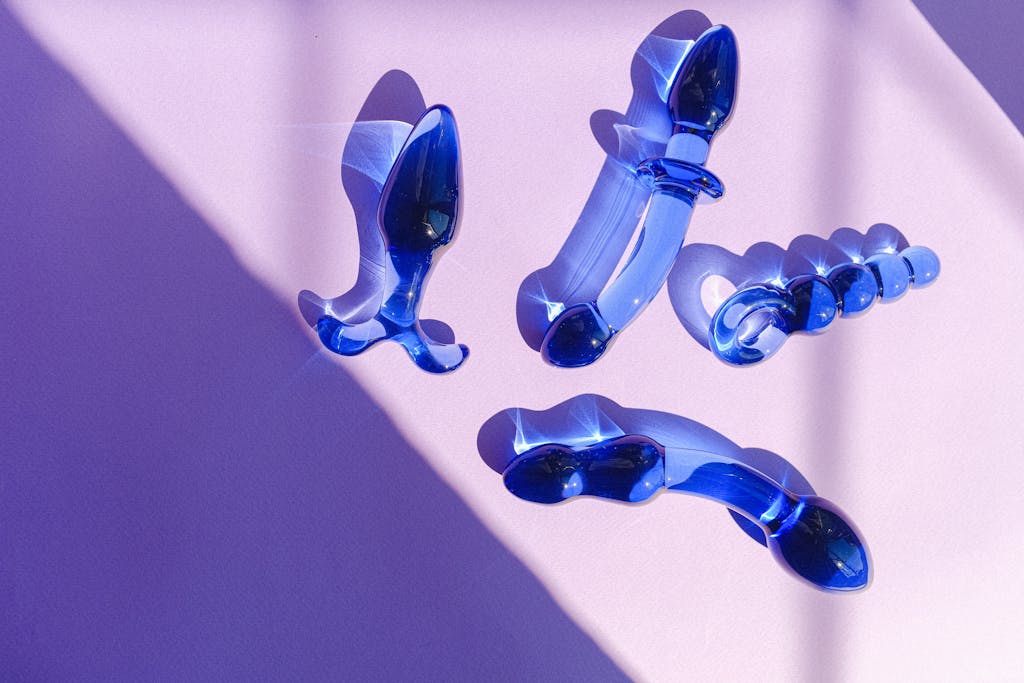 Artistic arrangement of blue glass adult toys on a purple backdrop, exuding elegance and modern style. sex toys in relationships and bedroom accessories