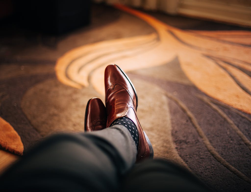 Close-up of polished brown leather shoes worn with patterned socks, relaxed indoors. men's style blog