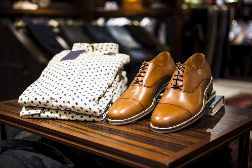 Elegant brown leather shoes and printed shirt displayed on a wooden table in a stylish clothing store. men's style blog