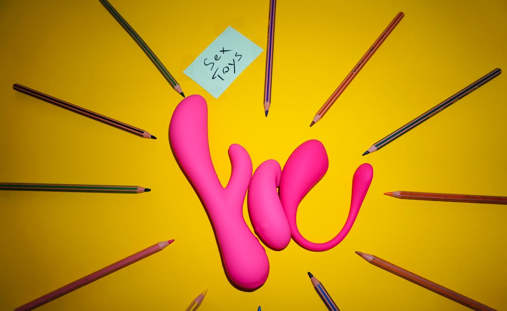 Pink sex toys surrounded by colored pencils on a yellow background. sex toys in relationships