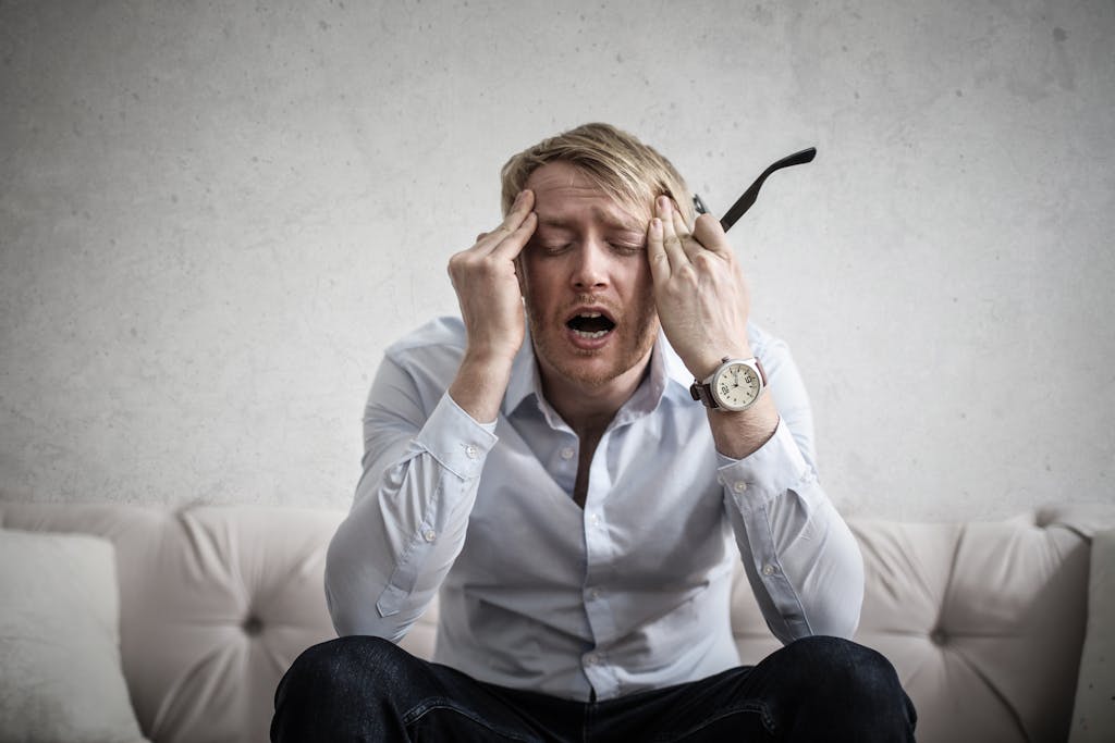 Stressed man sitting on couch, feeling overwhelmed and frustrated, expressing mental strain. financial stress in men