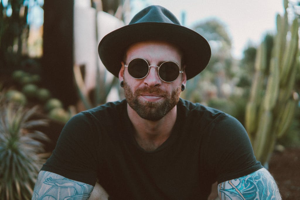 Stylish man with beard and tattoos wearing sunglasses and a hat, enjoying outdoors. sex education